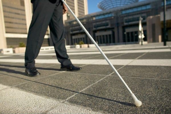 Person navigating a city sidewalk using a white cane